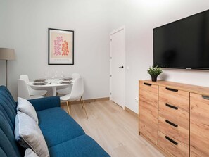 A modern living room with a sofa, dining table, chairs, a TV, and a cabinet.