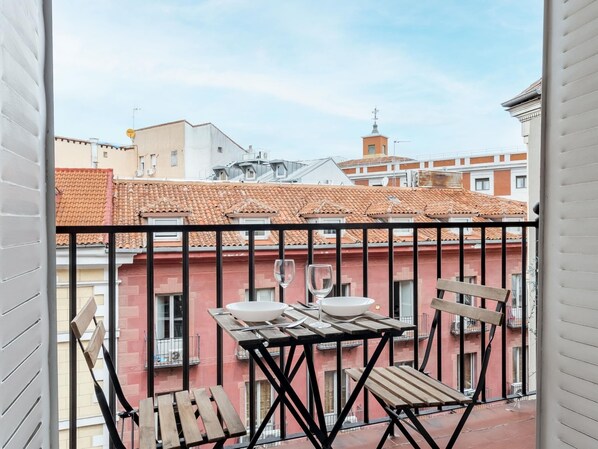 A balcony with a table and chairs, overlooking a red building with a tiled roof.