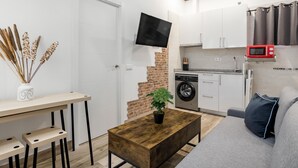 Un espace de vie compact comprenant un coin repas, un canapé, une table basse, un téléviseur, un lave-linge et un four à micro-ondes.
