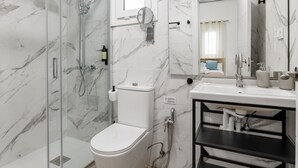 Une salle de bain moderne avec une douche à parois de verre, des toilettes blanches, un lavabo avec un miroir et un meuble-lavabo noir.