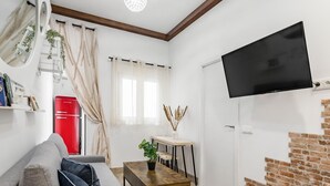 Un salon moderne avec un canapé gris, une table basse en bois, un réfrigérateur rouge, un téléviseur fixé au mur et une cheminée en briques.