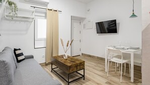 En moderne stue med en grå sofa, et træbord, et hvidt fjernsyn og et spiseområde med et hvidt bord og stole.