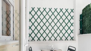 A small outdoor dining area with a table and two chairs, a lattice screen, and a window with patterned curtains. - Madrid Villaverde VI - Apartament with patio, AC (Madrid)