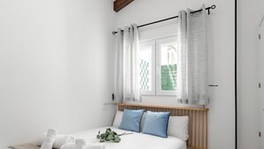 A bedroom with a bed, white bedding, a wooden headboard, a window with curtains, and a view of greenery outside. - Madrid Villaverde VI - Apartament with patio, AC (Madrid)