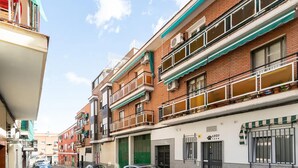 Uma rua estreita no centro da cidade, com edifícios altos, varandas e carros estacionados.