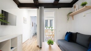 Una sala de estar moderna con un sofá, una mesa de centro con una planta, un televisor montado en la pared y piso de madera.