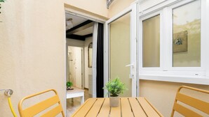 Un pequeño espacio al aire libre con una mesa y dos sillas, una ventana con vistas y una puerta que da a un baño.