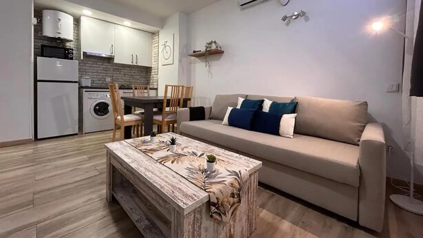 Una sala de estar moderna con un sofá color beige, una mesa de centro de madera y un comedor con una mesa y sillas.