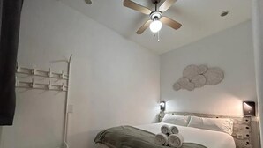 Un dormitorio con cama, ventilador de techo, luz empotrada en la pared y un elemento decorativo en la pared.