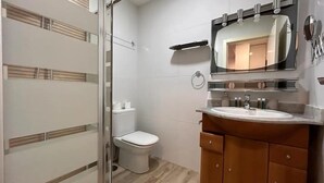 Un baño moderno con cabina de ducha de vidrio, inodoro, tocador con espejo y lavamanos.