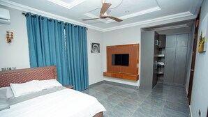 A bedroom with a bed, a ceiling fan, a TV mounted on the wall, and a wardrobe. - Gateway Lodge (Tamale)