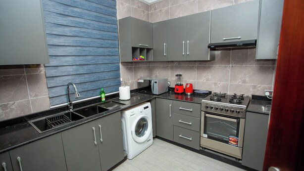 A modern kitchen with grey cabinets, a washing machine, a stove, and a microwave. - Gateway Lodge (Tamale)
