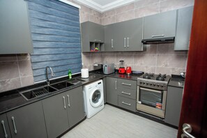 A modern kitchen with grey cabinets, a washing machine, a stove, and a microwave. - Gateway Lodge (Tamale)