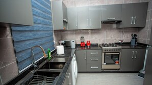 A modern kitchen with grey cabinets, a stainless steel sink, a dishwasher, a stove, and a microwave. - Gateway Lodge (Tamale)
