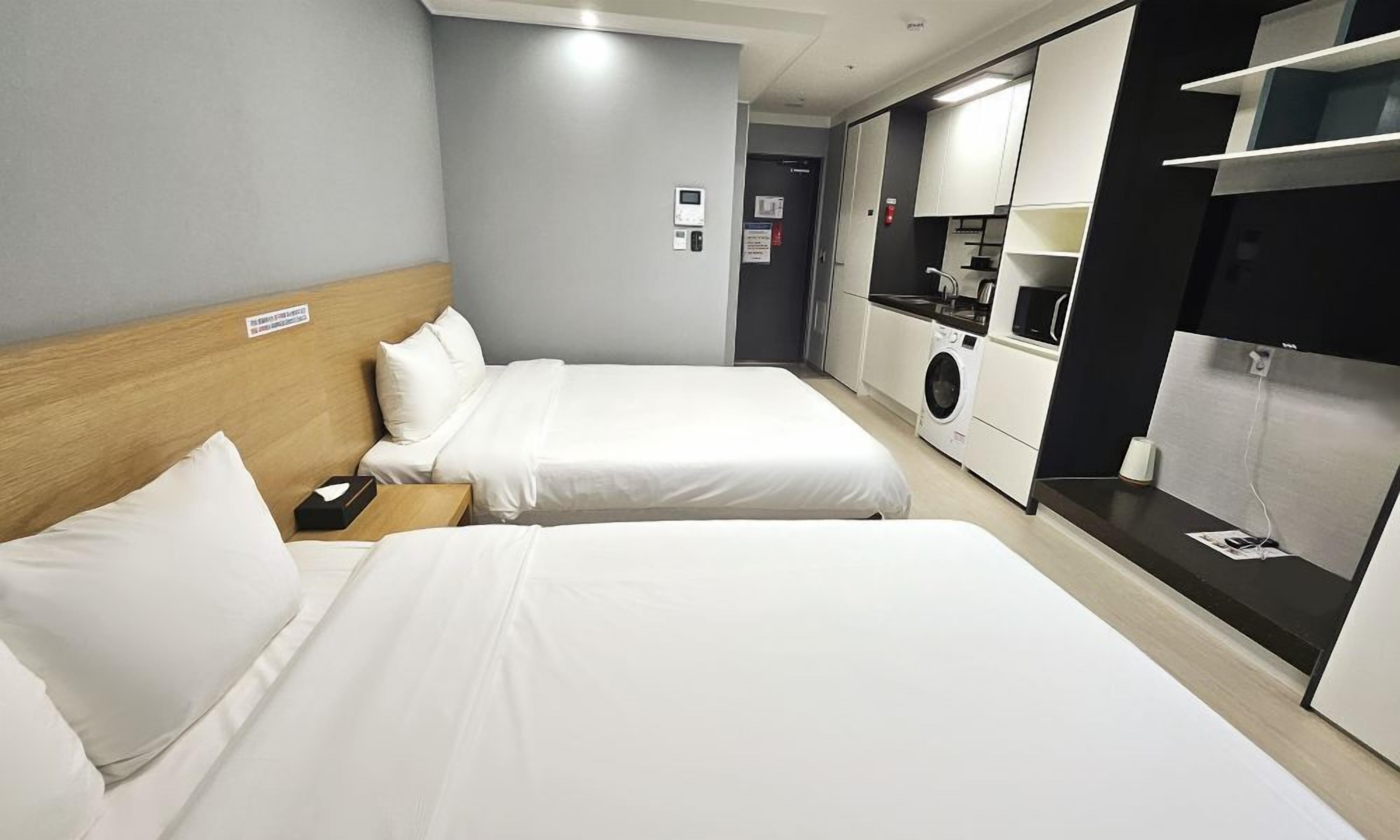 A hotel room with two beds, a washing machine, and a kitchenette.