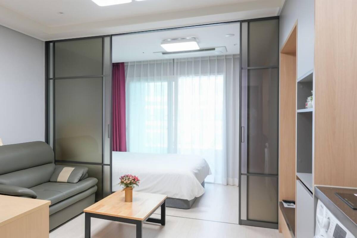 A modern hotel room with a sofa, a small table with a vase, a bed, and a sliding door leading to a balcony.