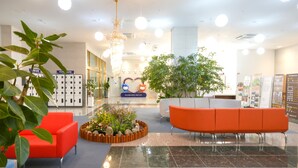 A hotel lobby with a reception desk, a large potted plant, and a red seating area. - FIRSTCITY HOTEL YEOSU (Yeosu)
