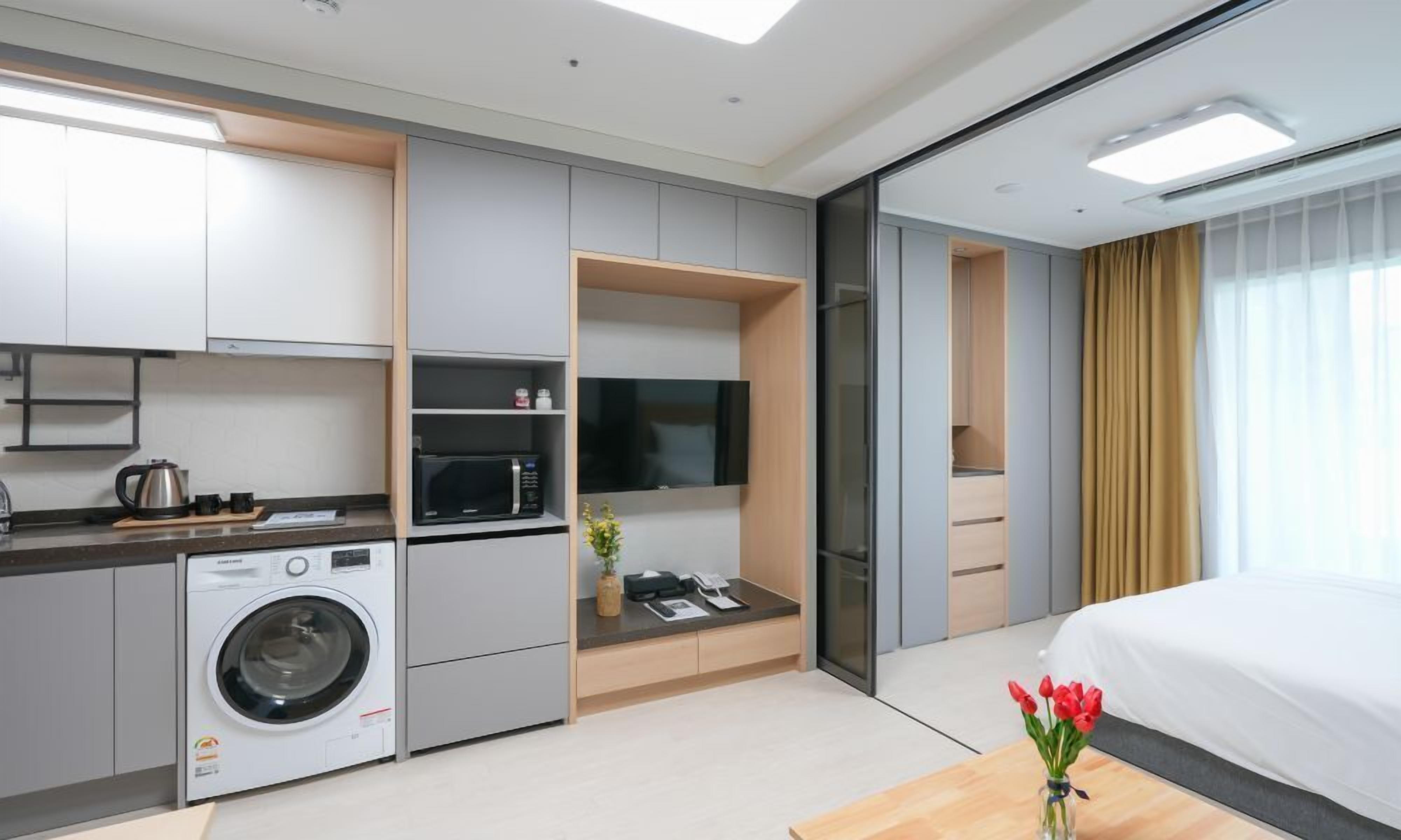 A modern hotel room with a washing machine, microwave, flat-screen TV, and a bed.