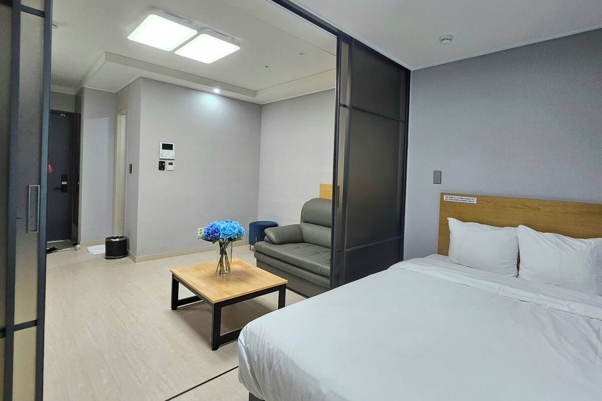 A hotel room with a bed, a wooden table with a vase of flowers, a grey sofa, and a blue chair.