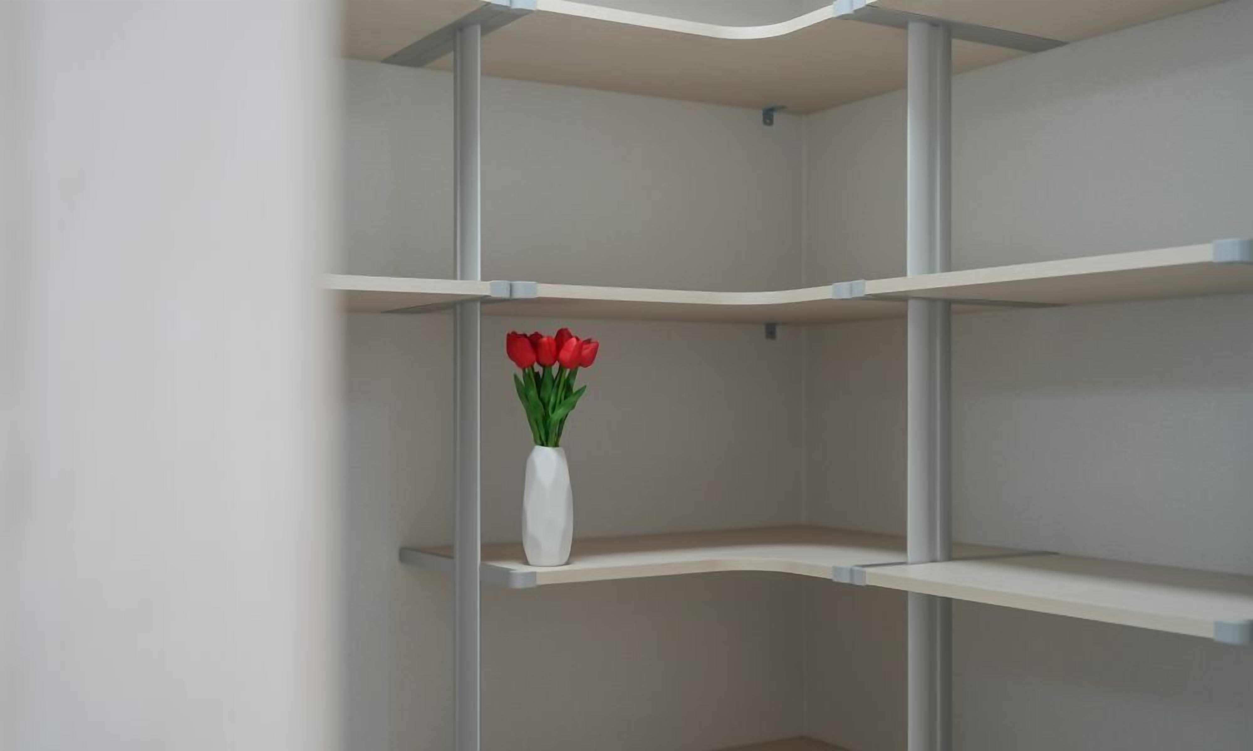 Una estantería blanca y vacía con un jarrón blanco que contiene flores rojas en una de sus repisas.