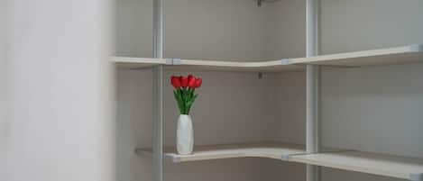 Una estantería blanca y vacía con un jarrón blanco que contiene flores rojas en una de sus repisas.