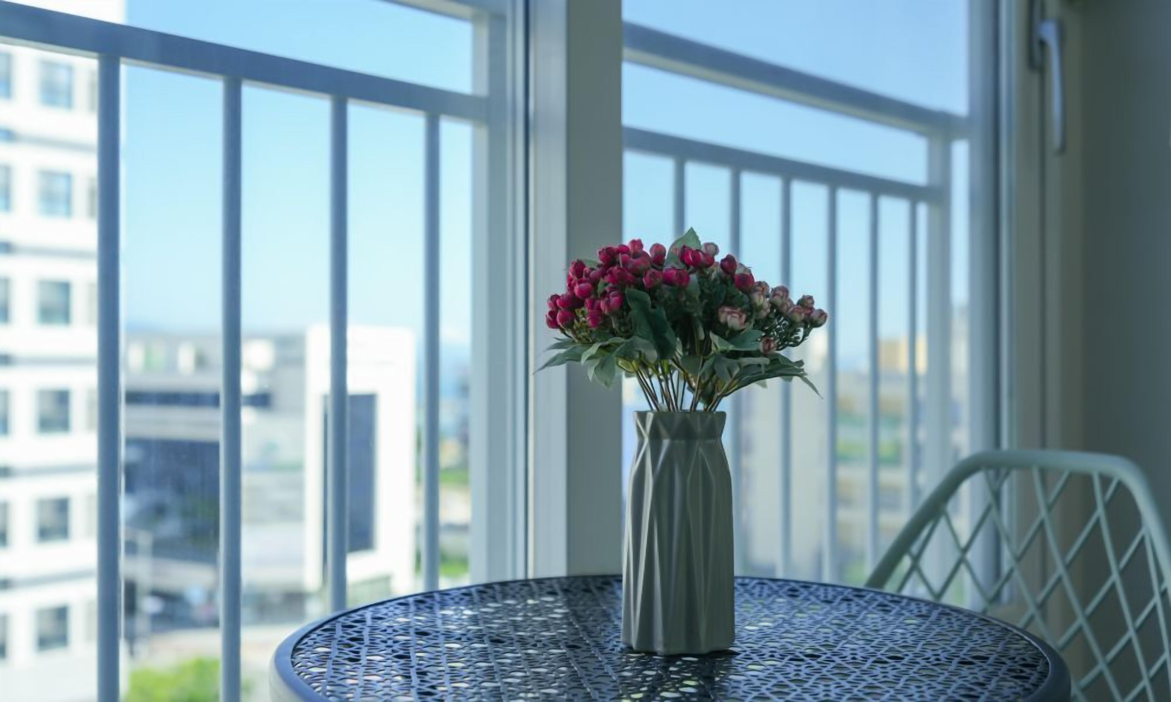 A balcony with a table, a vase with flowers, and a city view.