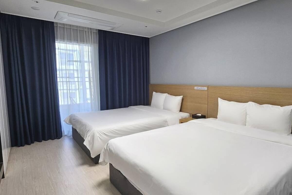 A hotel room with two beds, a wooden headboard, a nightstand, and a window with curtains.