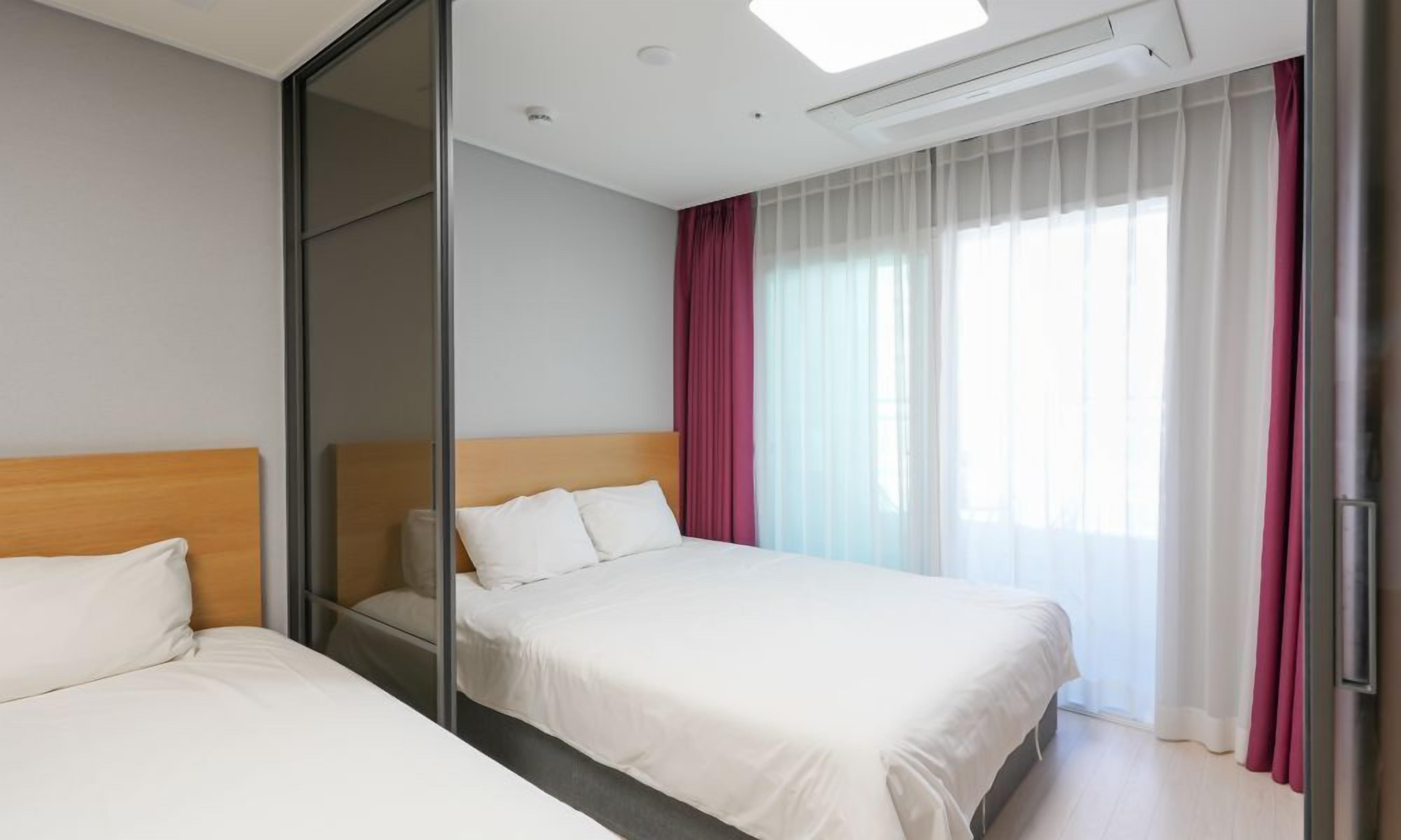 Ett hotellrum med två sängar, en skjutdörr, ett stort fönster med tunna gardiner och en taklampa.