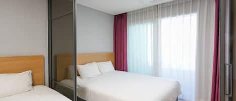 A hotel room with two beds, a sliding door, a large window with sheer curtains, and a ceiling light.
