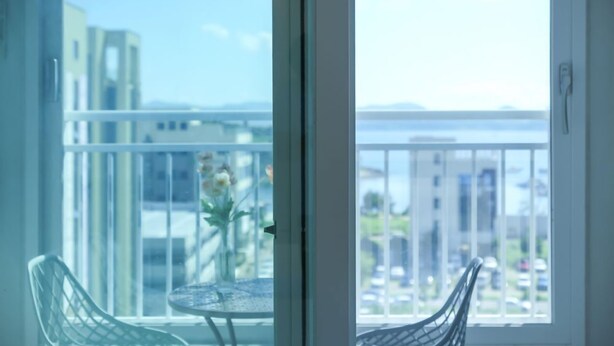 A balcony with a glass door, a small round table with a vase of flowers, and two wicker chairs. - FIRSTCITY HOTEL YEOSU (Yeosu)