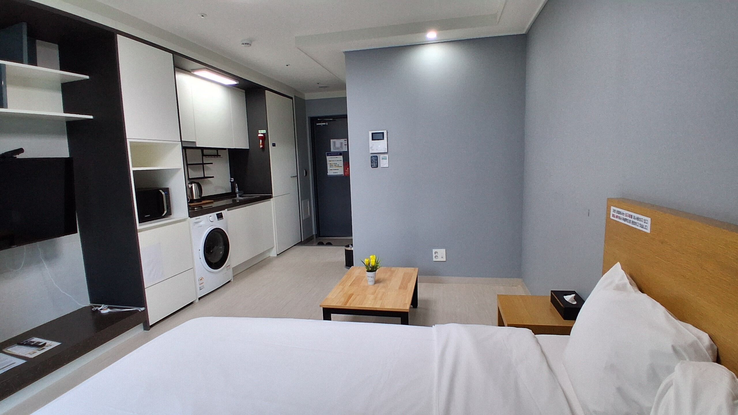Habitación de hotel con cama, una mesita, escritorio, lavadora y kitchenette.