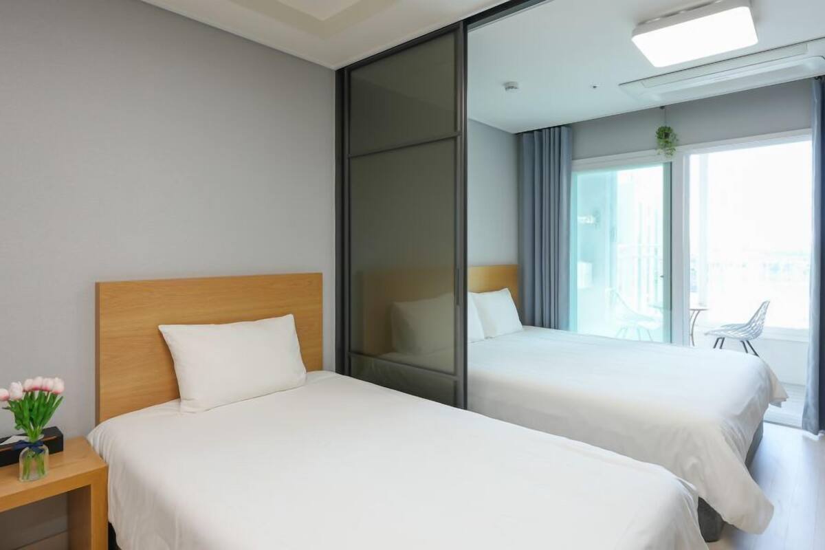 A hotel room with two beds, a nightstand, a mirror, and a view of the city through large windows.