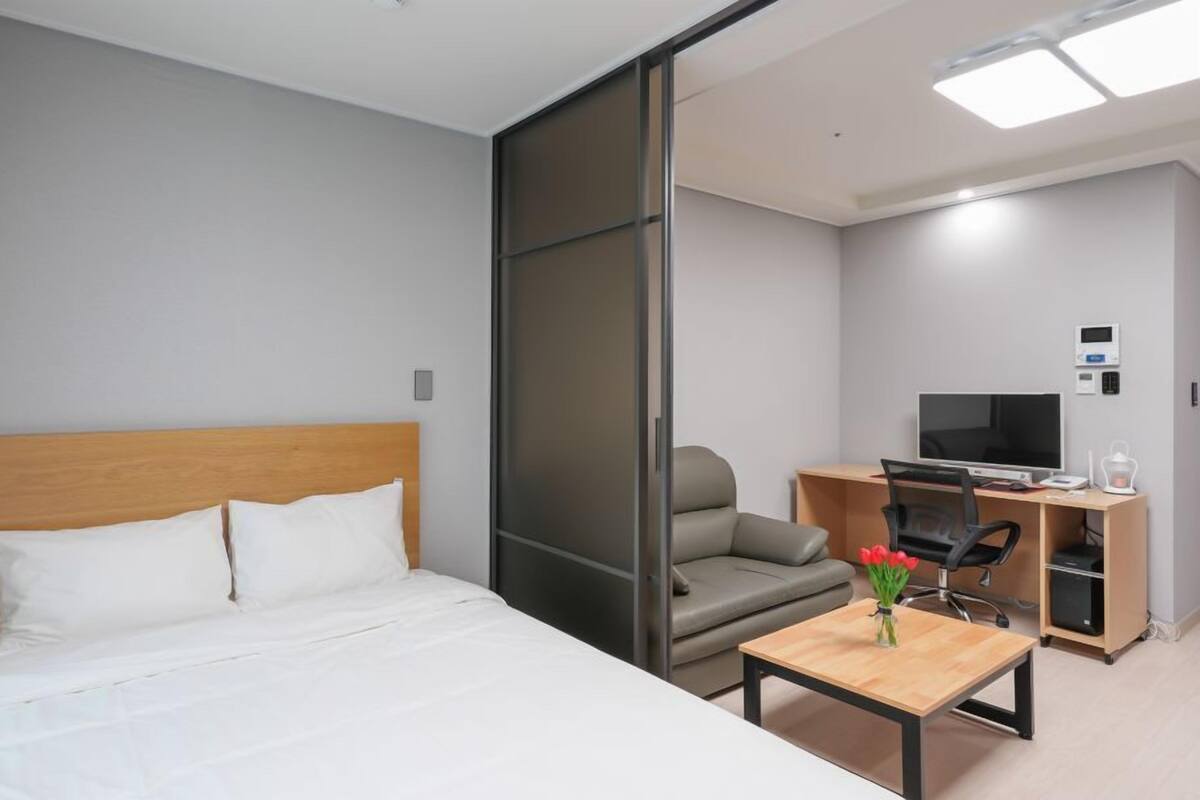 A hotel room with a bed, a desk, a chair, a TV, and a small table with flowers.