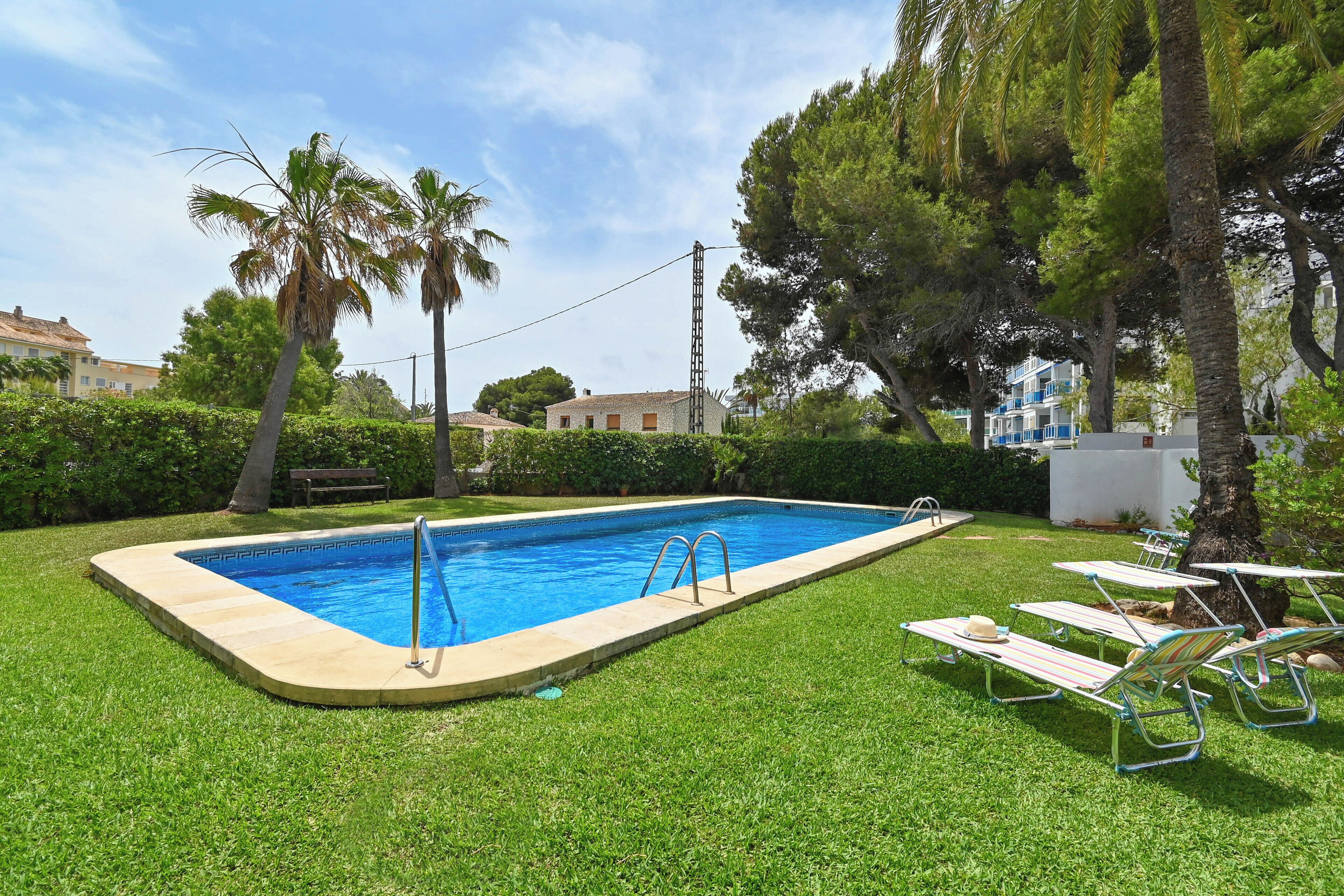 A rectangular swimming pool with a metal ladder, surrounded by a well-maintained lawn and several lounge chairs.