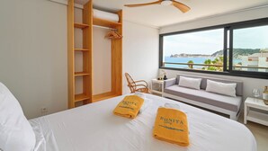 A hotel room with a bed, a wooden wardrobe, a seating area with a sofa and armchairs, and a large window offering a view of the sea. - Bonita Stay B Sun: Great views, new, fiber, airconditioning, pool, BBQ & parking (Bahia De Javea (Urbanizacion))