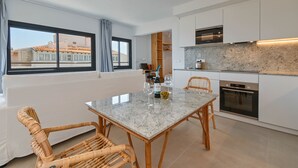 A modern kitchen with white cabinets, a granite countertop, and a built-in oven. There is a dining area with a table and wicker chairs. - Bonita Stay B Sun: Great views, new, fiber, airconditioning, pool, BBQ & parking (Bahia De Javea (Urbanizacion))