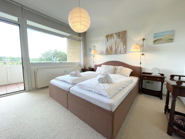 A neatly made bed with white linens and towels, a large window with a view, and a painting on the wall.