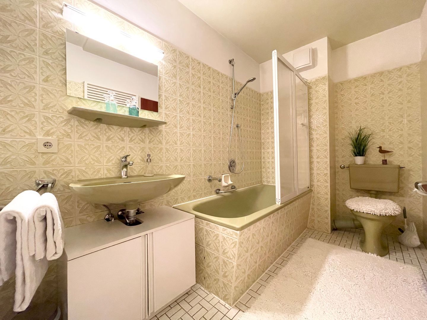 Ein Badezimmer mit Waschbecken, Badewanne und Dusche. Handtuchhalter und ein kleines Regal mit Pflegeprodukten sind vorhanden.