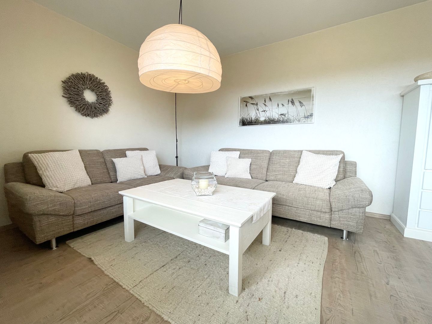 Ein Wohnzimmer mit zwei grauen Sofas, einem weißen Couchtisch, einer Pendelleuchte, einer Wandkrone und einem gerahmten Bild.