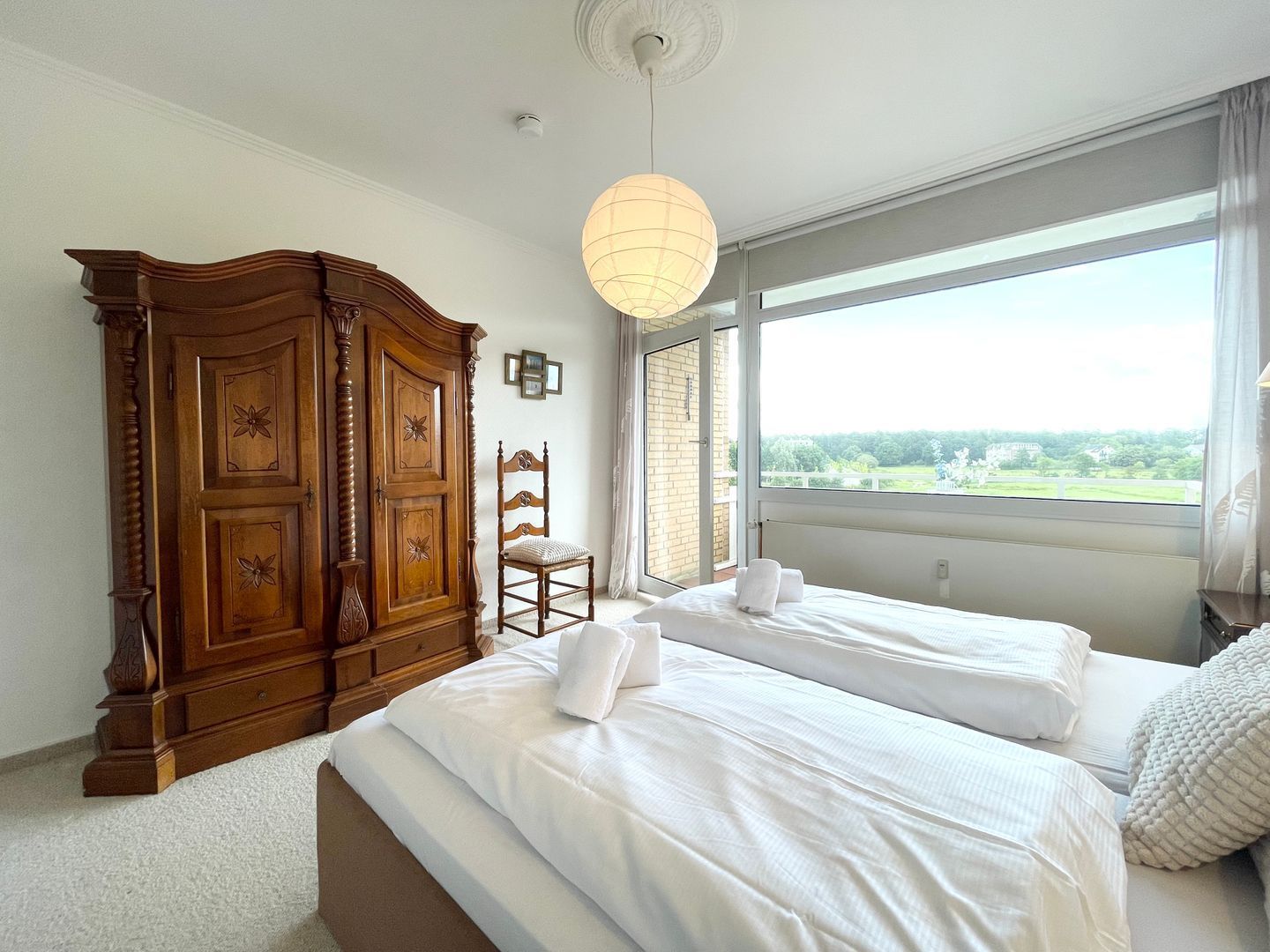Ein Schlafzimmer mit zwei Betten, einem Holzschrank, einem Stuhl und einem großen Fenster mit Blick.