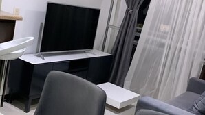 A modern living room with a flat-screen TV, a dining table, and grey sofas. - Luxurious Stay  (Bello)