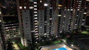 A high-rise residential building with multiple balconies, a swimming pool, and surrounding greenery. - Luxurious Stay  (Bello)