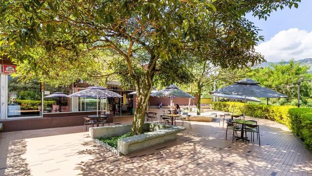 An outdoor patio area with tables and umbrellas, surrounded by greenery and a view of the cityscape. - Luxurious Stay  (Bello)