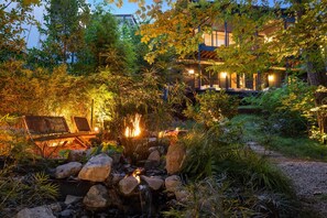 A garden with a water feature, rocks, and a building in the background.