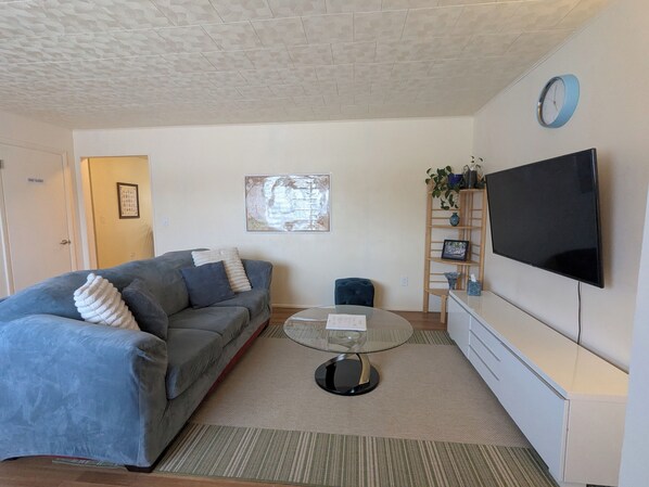 A living room with a sofa, a coffee table, a TV, a clock, and a bookshelf.