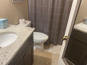 Un baño con inodoro blanco, lavamanos de mármol y cortina de ducha.