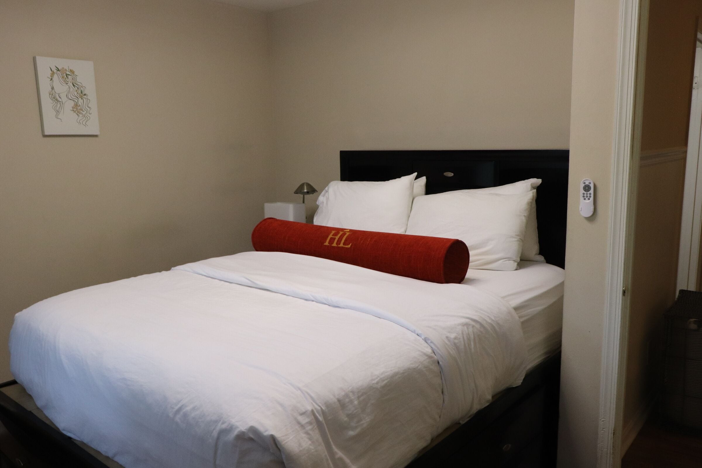 A hotel room with a bed, a nightstand, a lamp, and a wall-mounted remote control.
