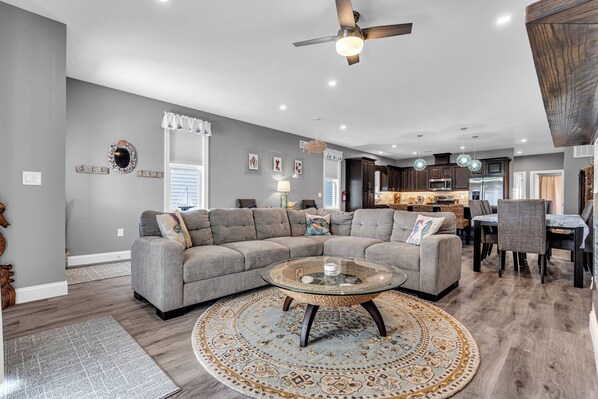Uma sala de estar moderna com um sofá seccional, uma mesa de centro de vidro e uma área de jantar com mesa e cadeiras.