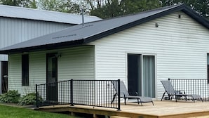 Ein Haus mit überdachter Veranda, einer Holzterrasse und zwei Liegestühlen.