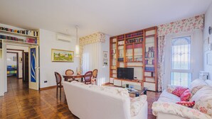 Ein Wohnzimmer mit einer Couch, einem Fernseher, einem Bücherregal und einem Essbereich mit Stühlen und einem Tisch.